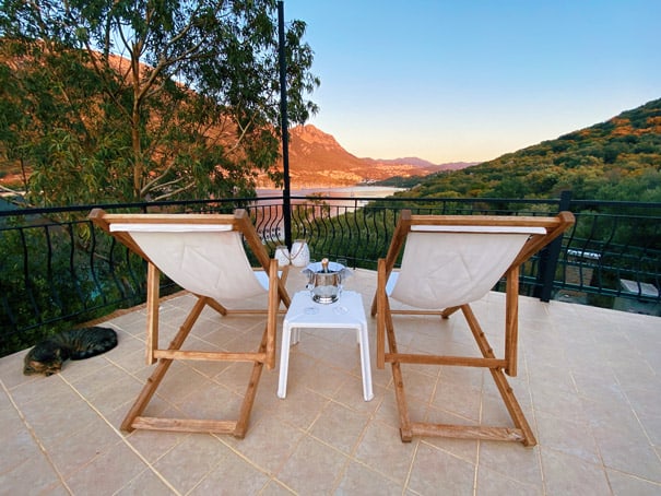 two white lounge chairs with champagne in ice bucket cat sleeping looking over Kas Setur Marina and yachts at sunset